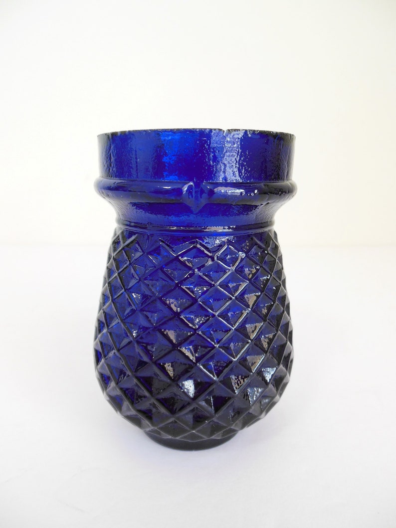 May include: A cobalt blue glass vase with a diamond pattern. The vase has a wide mouth and a rounded base.