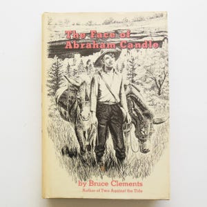 May include: A vintage book cover for "The Face of Abraham Candle" by Bruce Clements. The cover features a black and white illustration of a man in a hat standing with two donkeys in a grassy field. The title is in red letters.