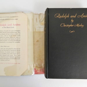 May include: A black book with gold lettering on the spine. The title is "Rudolph and Amina" by Christopher Morley. The back cover has a blurb about the book.