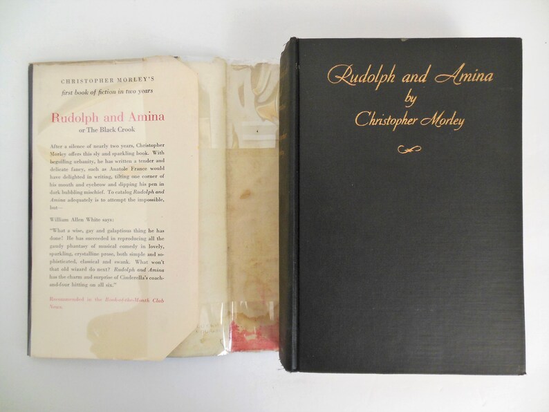 May include: A black book with gold lettering on the spine. The title is "Rudolph and Amina" by Christopher Morley. The back cover has a blurb about the book.