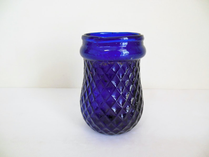 May include: A cobalt blue glass vase with a diamond pattern. The vase has a wide mouth and a rounded bottom.