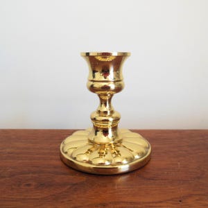 May include: A gold metal candle holder with a round base and a fluted design. The holder has a simple, elegant design.