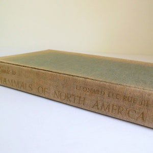 May include: A brown book with the title "Pictorial Guide to The Mammals of North America" by Leonard Lee Rue III.