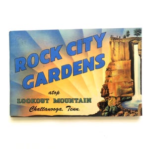 May include: Vintage postcard for Rock City Gardens atop Lookout Mountain in Chattanooga, Tennessee. The postcard features a scenic illustration of a waterfall and a blue and yellow sky with the text "Rock City Gardens".