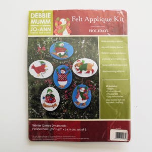 May include: A Debbie Mumm felt applique kit for holiday ornaments. The kit includes six oval-shaped ornaments with winter-themed designs, such as snowmen and a cardinal. Finished size is 3.5" x 4.5" (9 x 11 cm).