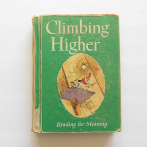 May include: A green book with the title "Climbing Higher" and the subtitle "Reading for Meaning". The cover features an illustration of a dog wearing a party hat, standing on a platform with a ladder.