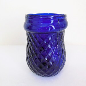 May include: A cobalt blue glass vase with a diamond pattern. The vase has a wide mouth and a rounded bottom.