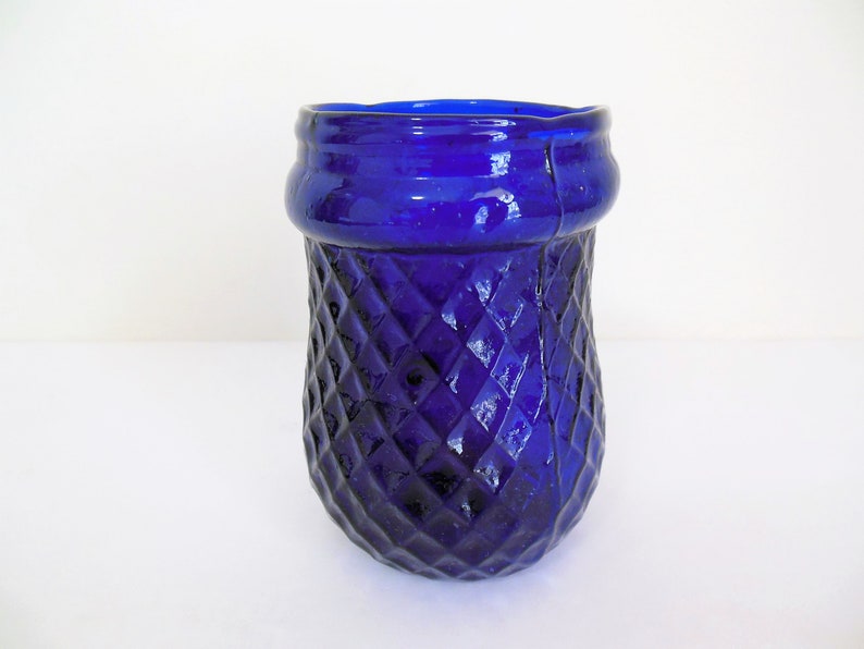 May include: A cobalt blue glass vase with a diamond pattern. The vase has a wide mouth and a rounded bottom.