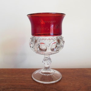 May include: A clear glass goblet with a red glass top. The top is etched with the words "Souvenir Traverse City, Mich".