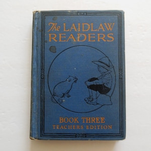 May include: Vintage "The Laidlaw Readers" book. The cover is blue with orange text and a circular illustration of a child and a cat. The book is titled "Book Three Teachers Edition".