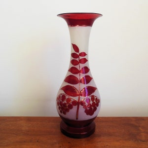 May include: A white frosted glass vase with a red rim and base. The vase has a red and gold floral design with leaves and berries.