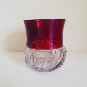 May include: A clear glass vase with a ruby red top. The vase has a decorative, swirling pattern around the bottom.