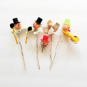 May include: Five vintage Christmas tree toppers. Two are snowman figures with black top hats, one is an angel with gold wings, one is a red-hatted figure with a smiling face, and one is a yellow-haired figure with a green top hat.