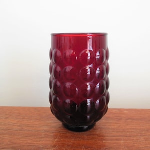 May include: A deep red glass tumbler with a textured, bubble-like design. The glass is clear and has a rounded bottom.