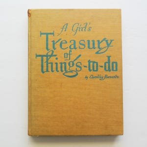 May include: A yellow book with the title "A Girl's Treasury of Things-to-do" in teal lettering. The author is listed as Caroline  Howardz.
