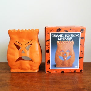 May include: Orange ceramic pumpkin luminaria with a carved angry face. The pumpkin is packaged in a box with a picture of a smiling pumpkin luminaria and the text "Ceramic Pumpkin Luminaria".