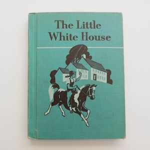 May include: A vintage book cover with a teal background. The title "The Little White House" is printed in black. The cover features a black and white illustration of a girl riding a horse in front of a white house.