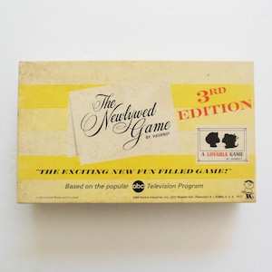 May include: Vintage "The Newlywed Game" board game box. The box is yellow and cream-colored with the game title in elegant script. The box reads "3rd Edition" and "A Lovable Game".
