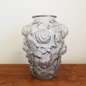 May include: A clear glass vase with a textured surface, featuring raised floral designs in the shape of roses.
