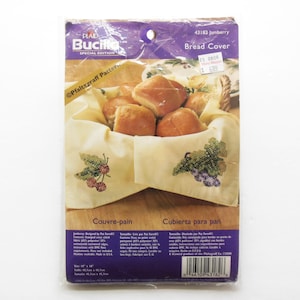 May include: A cross-stitch pattern for a bread cover featuring a basket of rolls and a design of cherries and grapes. The pattern is from Plaid Bucilla's Special Edition collection and is called "Jamberry".