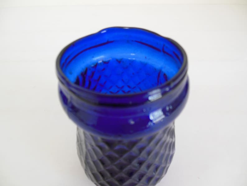 May include: A cobalt blue glass vase with a diamond pattern. The vase has a wide mouth and a rounded base.