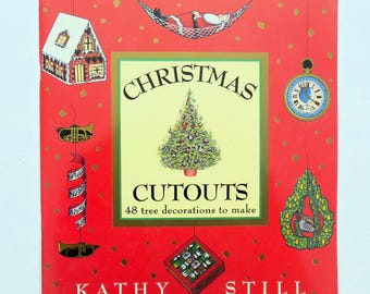 May include: A red book cover with the title "Christmas Cutouts" and the subtitle "48 tree decorations to make". The cover features illustrations of a gingerbread house, a Christmas tree, a Santa Claus in a hammock, a clock, and a musical note.