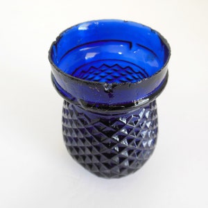 May include: A cobalt blue glass candle holder with a diamond pattern. The holder has a slightly chipped rim.