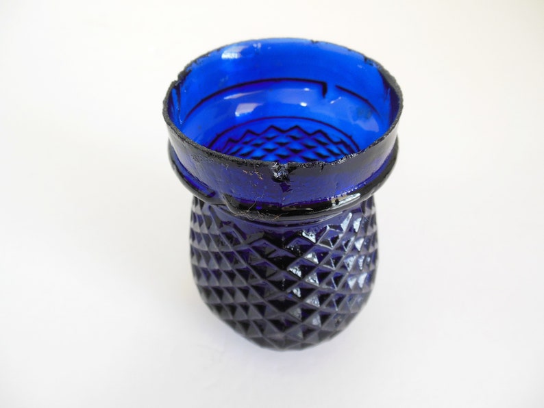 May include: A cobalt blue glass candle holder with a diamond pattern. The holder has a slightly chipped rim.