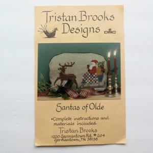 May include: A cross-stitch pattern for a Christmas scene featuring Santa Claus riding in a sleigh pulled by a reindeer. The pattern is titled "Santas of Olde" and includes complete instructions and materials. It is designed by Tristan Brooks.