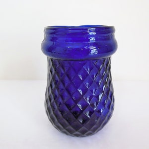 May include: A cobalt blue glass vase with a diamond pattern. The vase has a wide mouth and a rounded bottom.