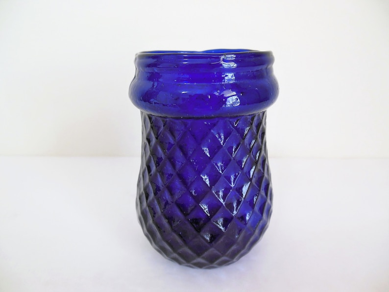 May include: A cobalt blue glass vase with a diamond pattern. The vase has a wide mouth and a rounded bottom.