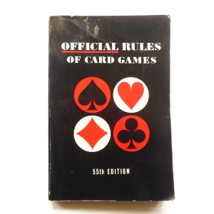 May include: A black book with the title "OFFICIAL RULES OF CARD GAMES" in white text. The cover features four playing card symbols: a spade, a heart, a diamond, and a club. The book is the 55th edition.