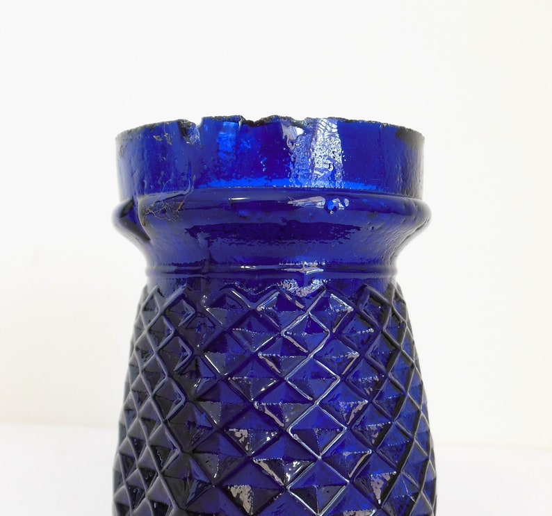 May include: A cobalt blue glass vase with a diamond pattern. The vase has a wide mouth and a narrow base.
