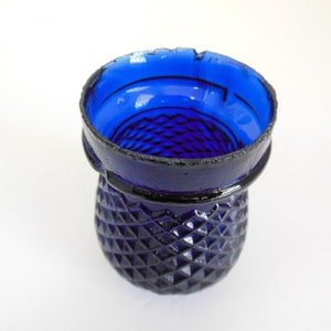 May include: A cobalt blue glass vase with a diamond pattern. The vase has a wide mouth and a rounded base.