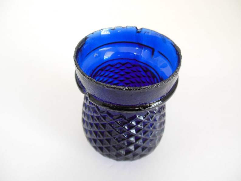 May include: A cobalt blue glass vase with a diamond pattern. The vase has a wide mouth and a rounded base.