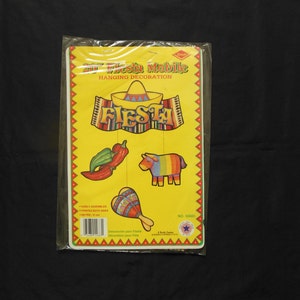 May include: A yellow and red cardboard hanging decoration with the word "Fiesta" in a colorful banner. The decoration includes a sombrero, a chili pepper, and a bull. The package includes instructions for assembly and is labeled "Fiesta Mobile Hanging Decoration".