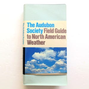 May include: A light blue book titled "The Audubon Society Field Guide to North American Weather." The book has a sky and cloud image on the cover. The book is rectangular and has a light blue cover.