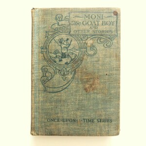 May include: Vintage book titled "Moni the Goat Boy and Other Stories" with a light blue cover. The cover features ornate teal lettering and illustrations, with the words "Once Upon a Time Series" at the bottom. The book shows signs of age and wear.
