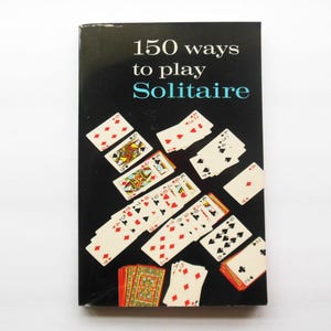 May include: A book cover with the title "150 ways to play Solitaire" in white and teal text on a black background. Playing cards are scattered around the title, showcasing various suits and card values.