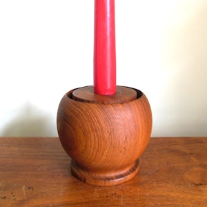 May include: A wooden candle holder with a round base and a red candle. The holder is made of teak wood and has a natural finish.