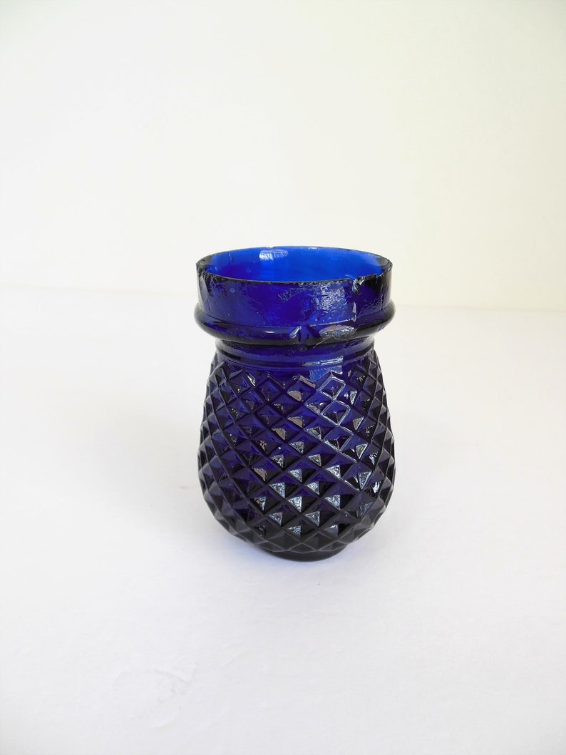 May include: A small, cobalt blue glass vase with a diamond-shaped pattern. The vase is about 4 inches tall and has a wide mouth.