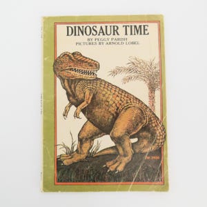 May include: A vintage children's book titled "Dinosaur Time" by Peggy Parish with illustrations by Arnold Lobel. The cover features a green, brown, and yellow dinosaur with a palm tree in the background.