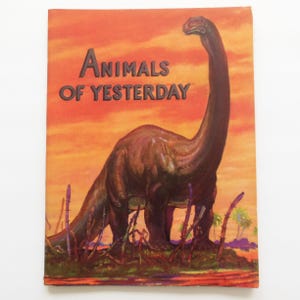 May include: A vintage book cover titled "Animals of Yesterday" featuring a brown dinosaur against an orange and yellow sunset backdrop. The dinosaur has a long neck and is standing on a patch of green grass with purple plants.