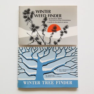 May include: Two vintage guidebooks: "Winter Weed Finder" and "Winter Tree Finder." The top book features a gray cover with black botanical illustrations and an orange sun. The bottom book has a blue cover with a stylized tree design.