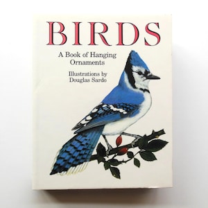 May include: A book titled "BIRDS" with a blue jay illustration. The cover features the title in pink, with the subtitle "A Book of Hanging Ornaments" and the author's name, Douglas Sardo.