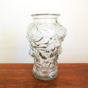 May include: A clear glass vase with a textured surface featuring raised rose designs. The vase is approximately 7 inches tall.