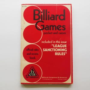 May include: A rectangular softcover book titled Billiard Games pocket and carom with a red cover featuring white circles and black text. The cover includes the text $1.25, official rules and record book, and League Sanctioning Rules.