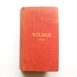 May include: A red hardcover book with the title "WILBER" and the year "1909" printed in gold lettering.