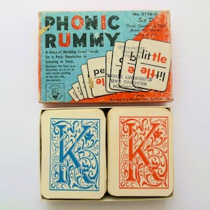 May include: A vintage Phonic Rummy game box with two cards showing the letter K in blue and red. The box is labeled "Phonic Rummy" and has the text "A Game of Matching Vowel Sounds for a Basic Foundation in Learning to Read."