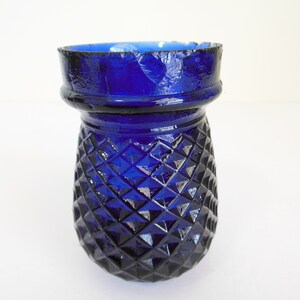 May include: A cobalt blue glass vase with a diamond pattern. The vase has a slightly chipped rim.
